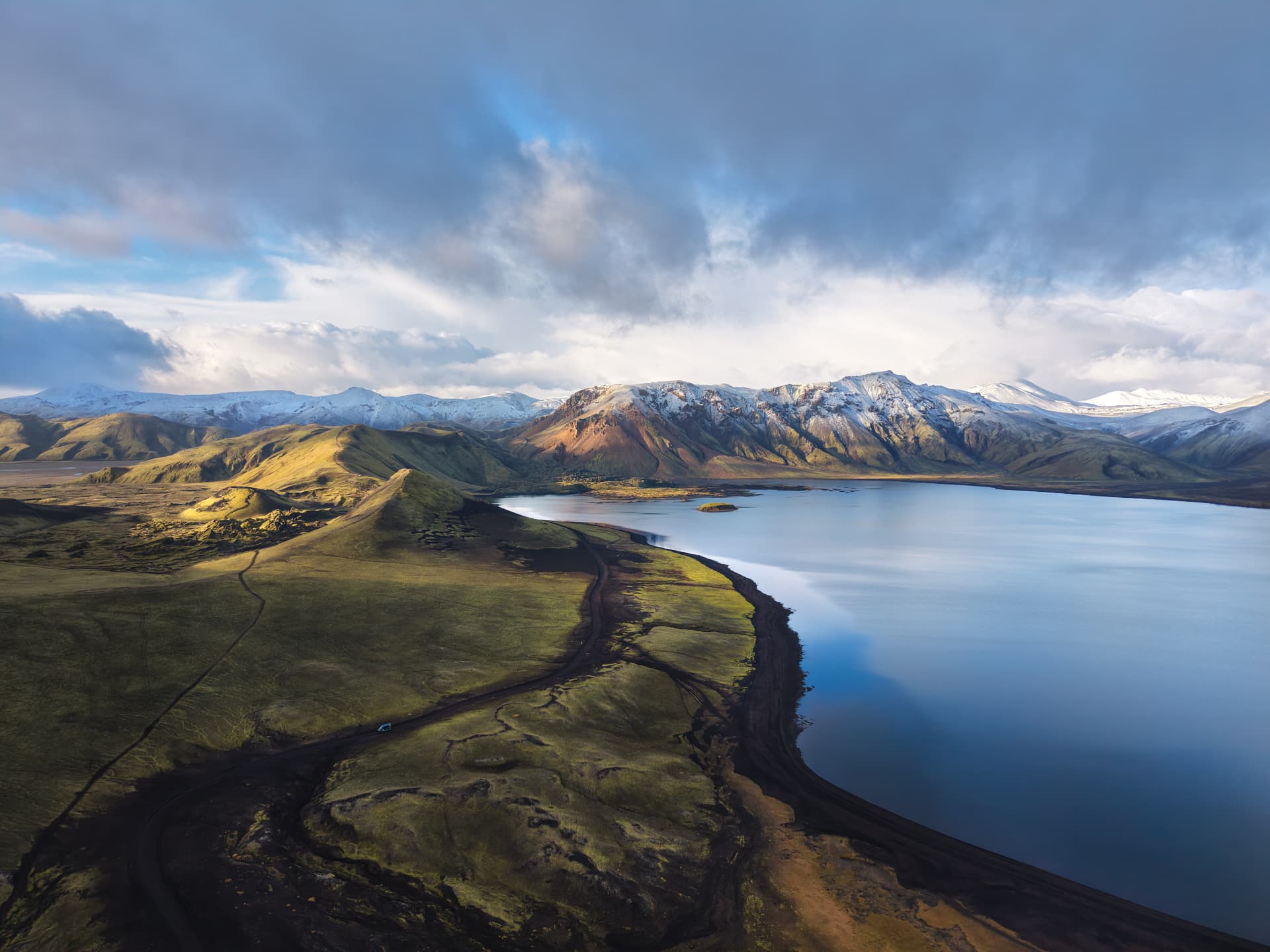 A drone view over the Highlands near Landmannalaugar, with our van tiny on the dirt road beside a still lake and snow dusted mountains