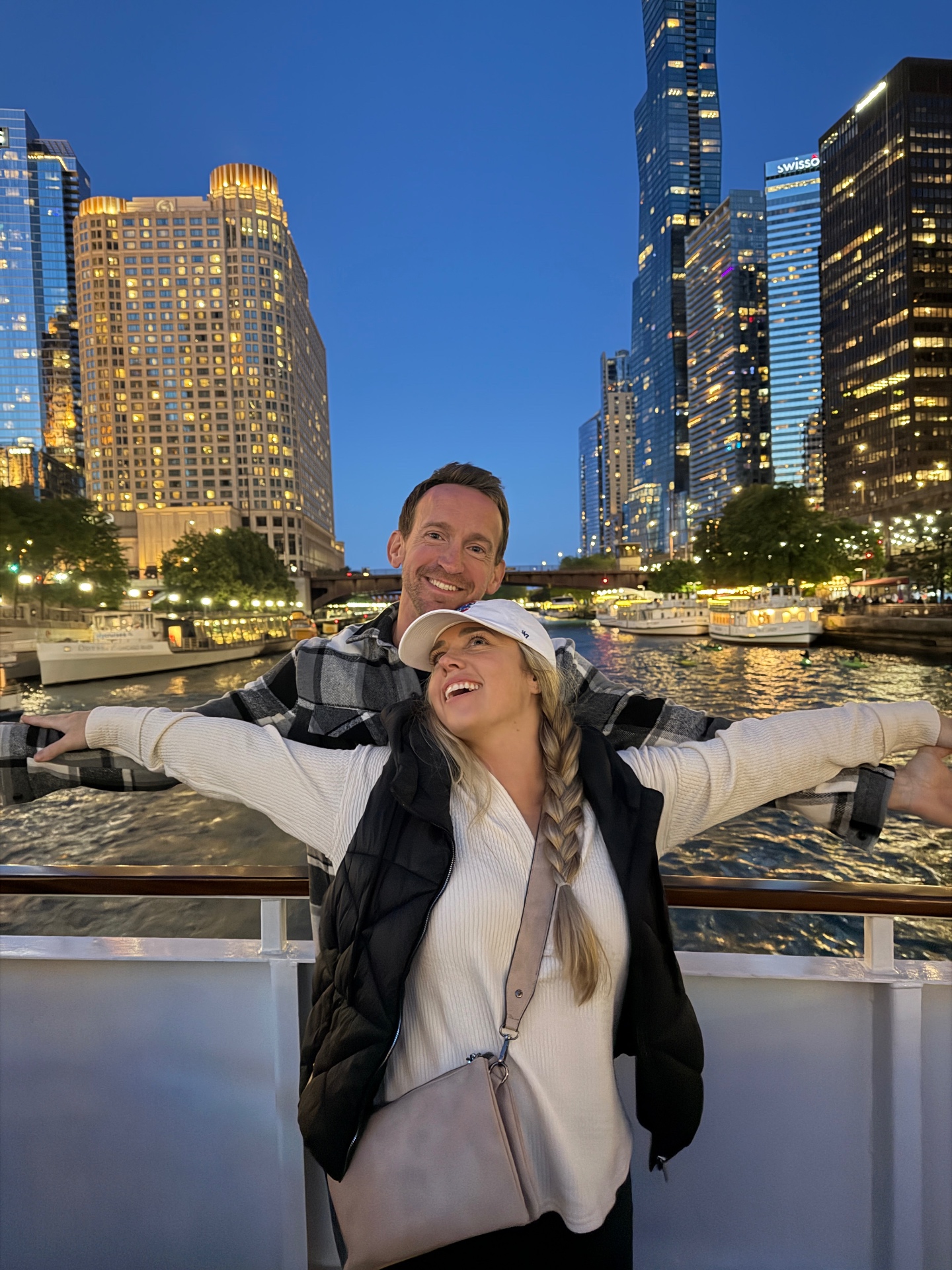 Brittany and Jake laughing on a boat with the Chicago skyline lit up behind them at dusk