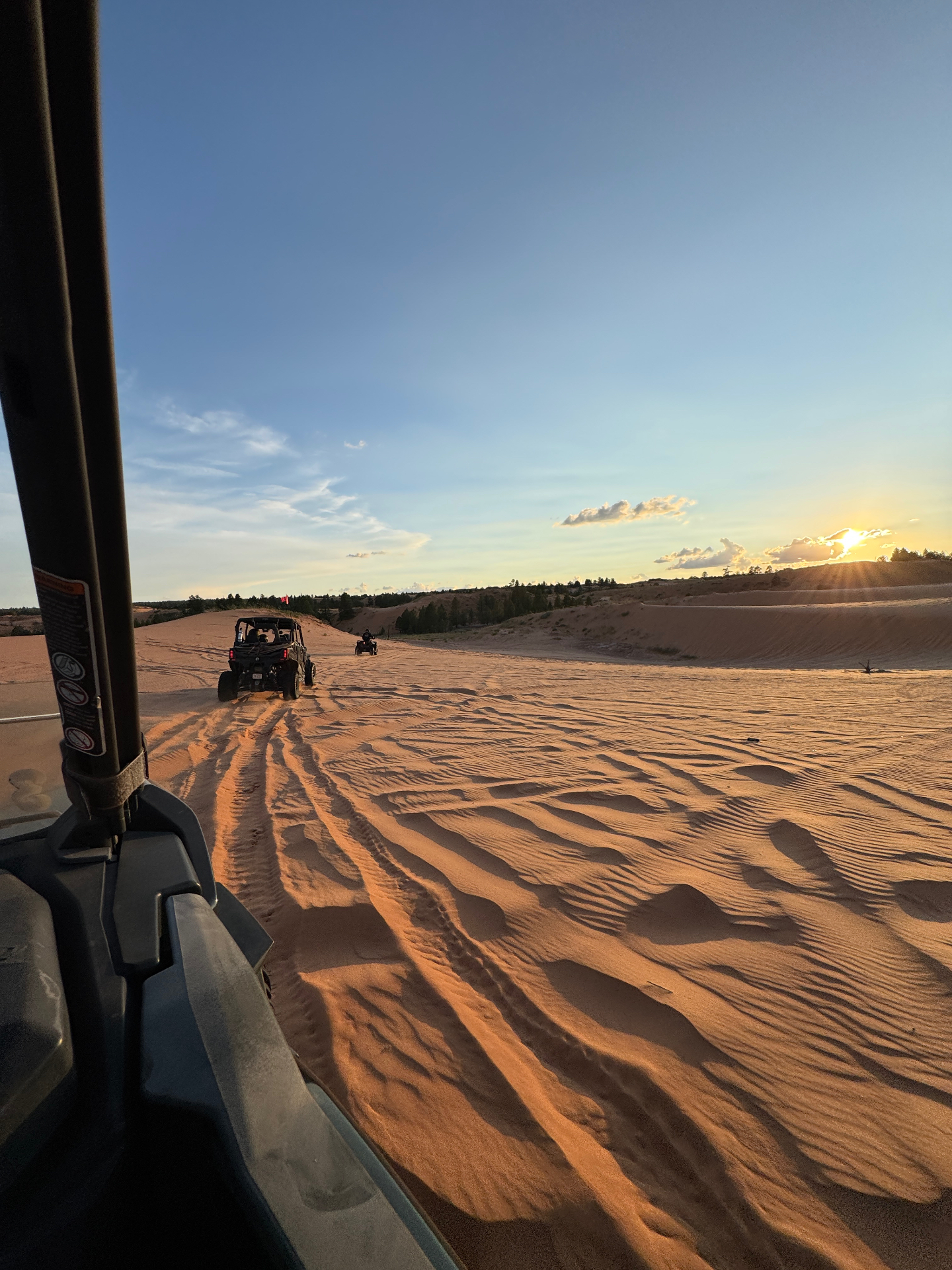 View from inside the UTV looking out at the convoy of side-by-sides rolling across the rippled Coral Pink sand dunes at golden hour