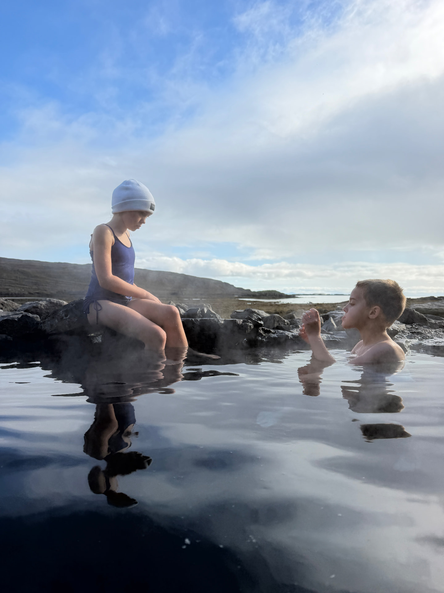 Aniston and Noah soaking in a steaming natural hot spring by the sea, one of our favorite hidden gems from the trip