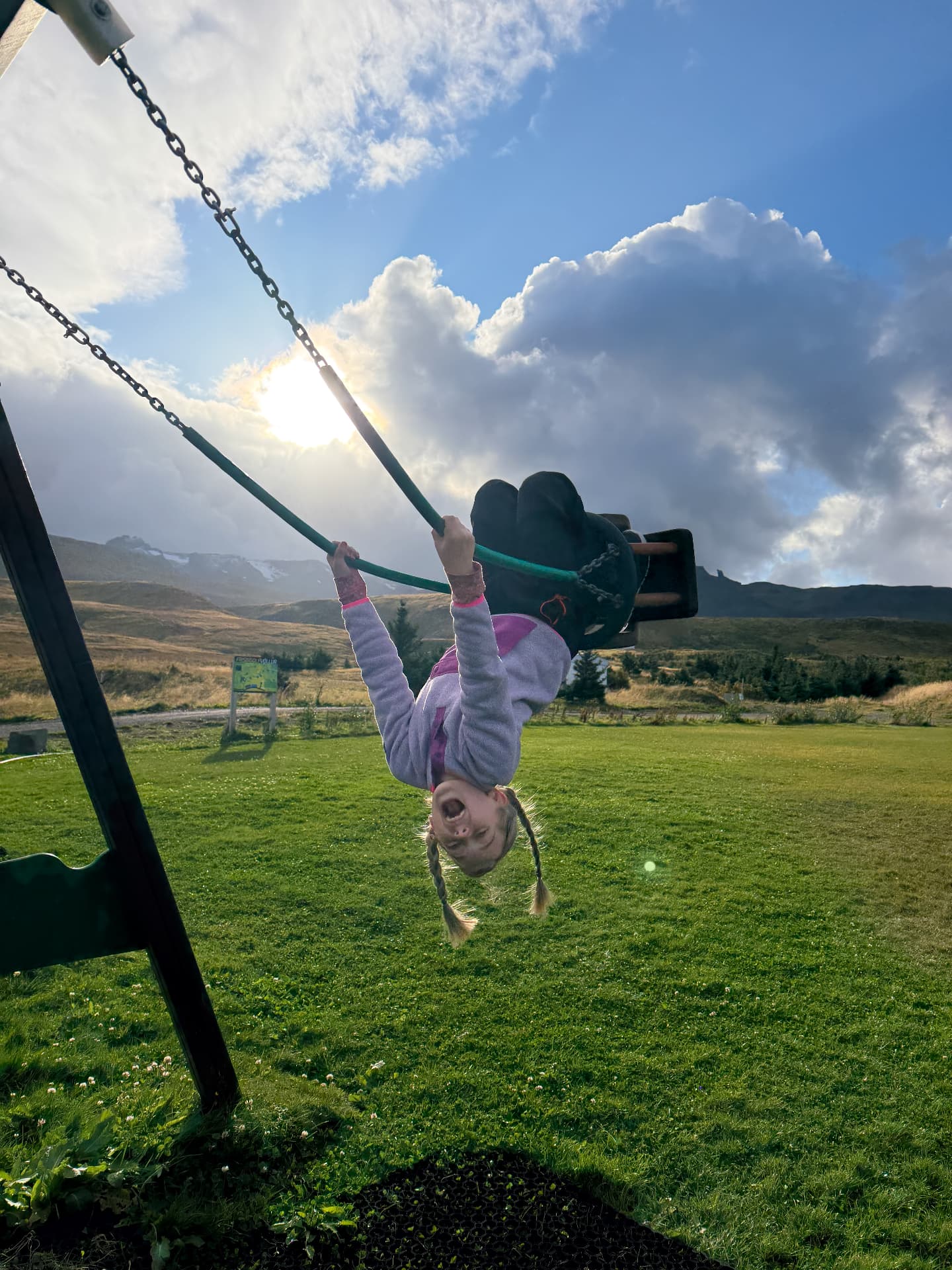 Aniston hanging upside down on a swing at one of Iceland's many small town playgrounds, mountains and all