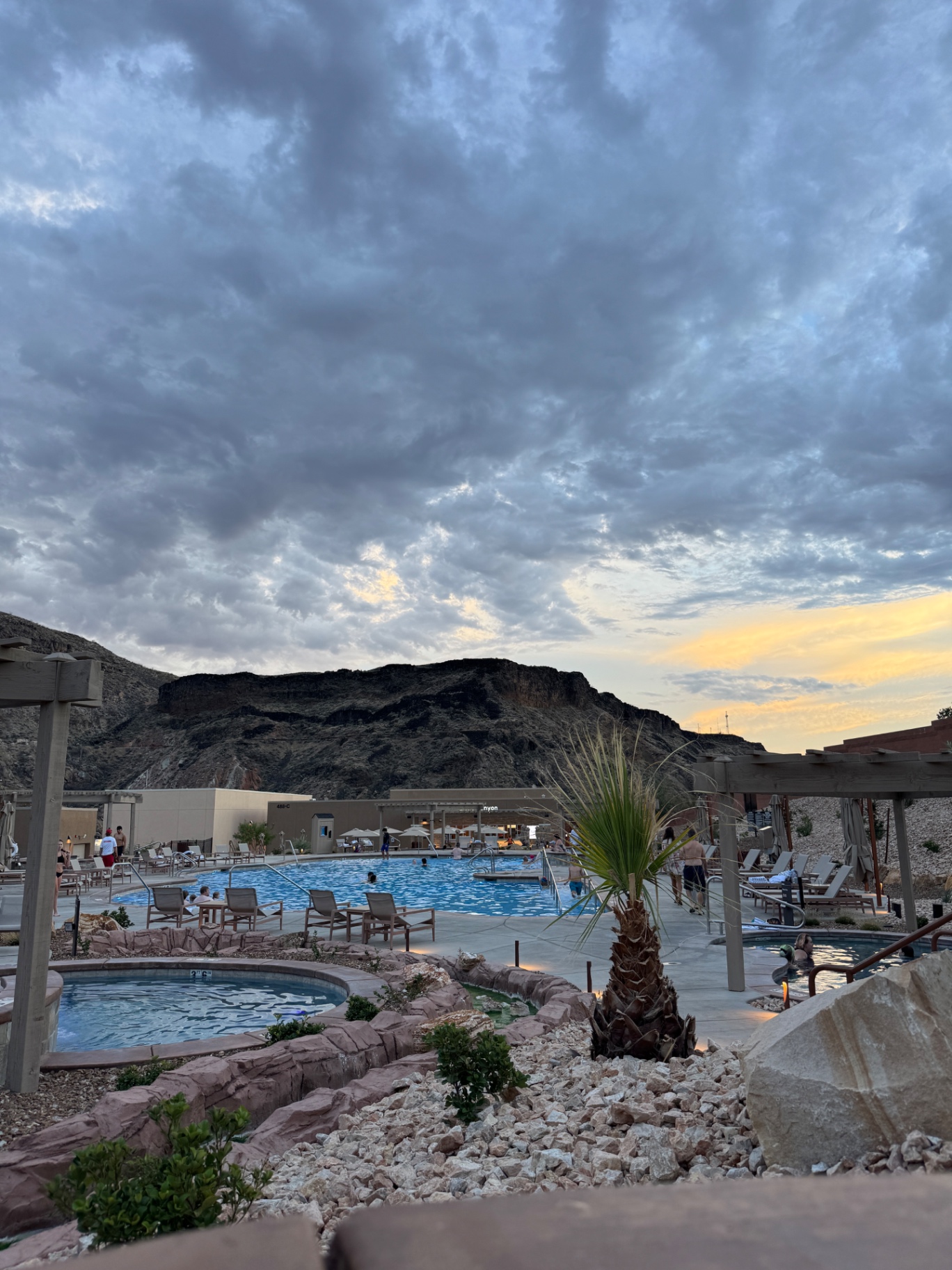 Zion Canyon Hot Springs resort at sunset with mineral pools, red rock cliffs, and a moody Utah sky overhead