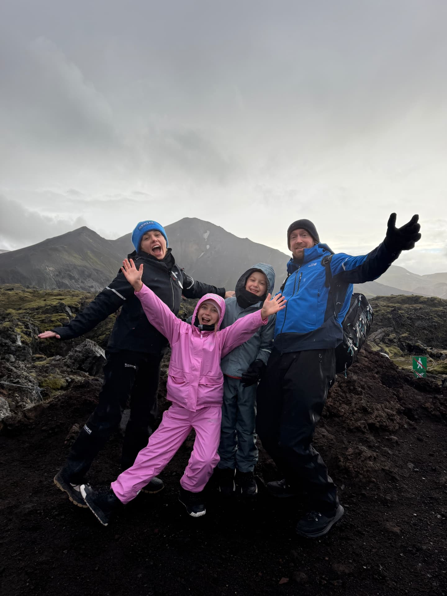 All four of us celebrating on a rocky volcanic hillside in the Highlands, arms up and completely soaked but so happy