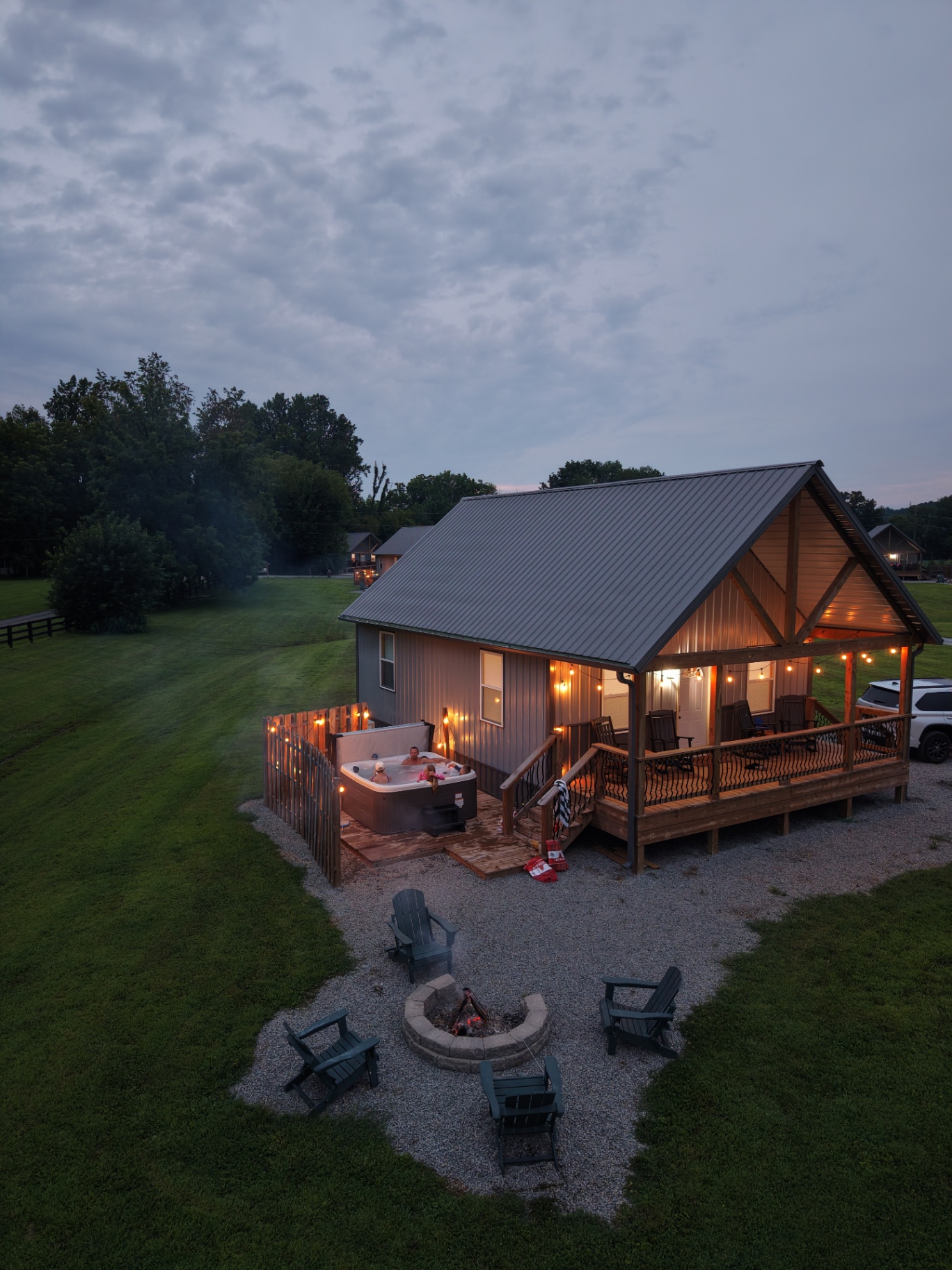 Aerial dusk view of a Cabins on the Cumberland cabin with hot tub, string lights, and a lit firepit