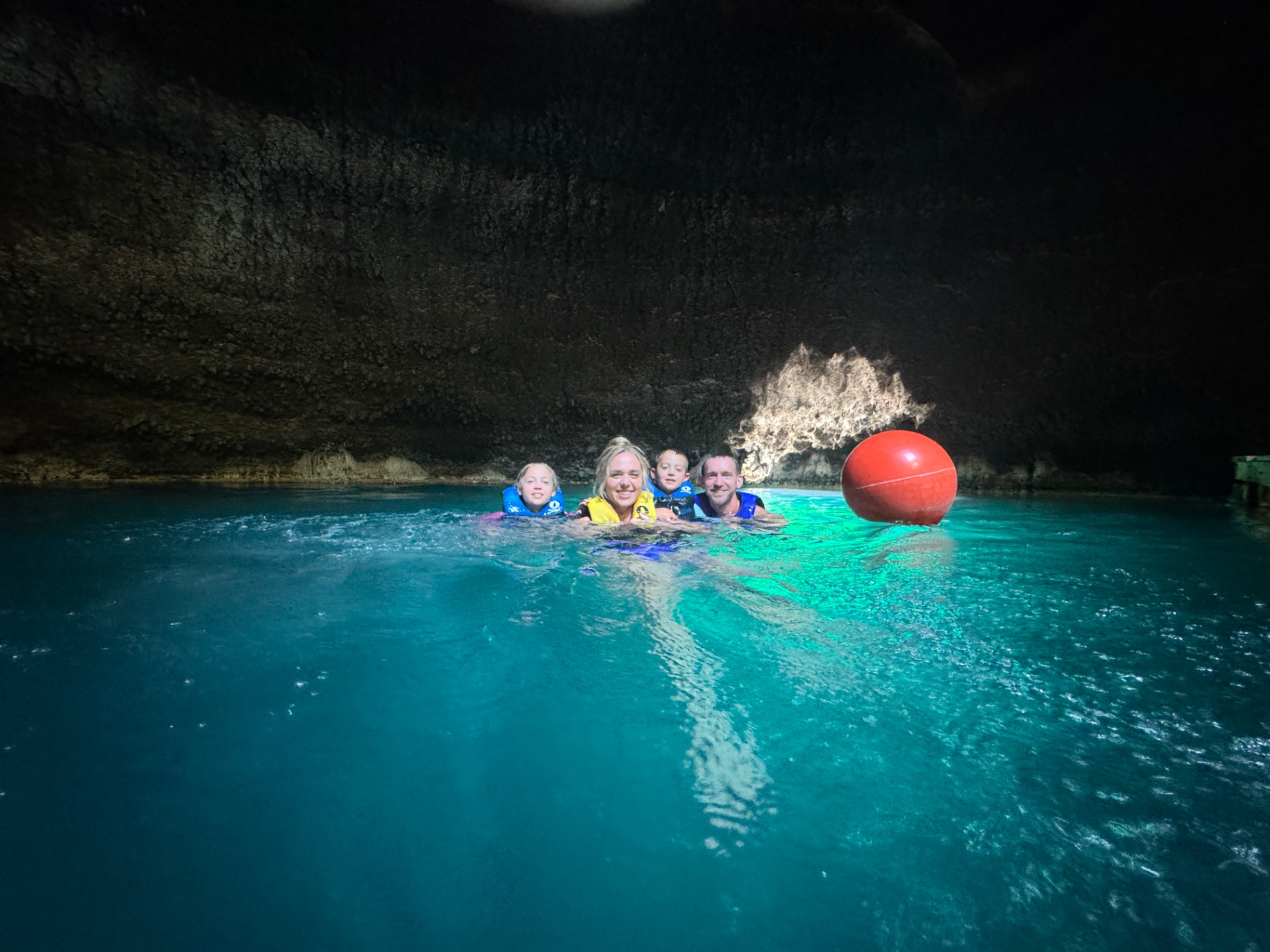 The Venture Seekers family in life jackets smiling together inside the Homestead Crater with sunlight breaking through the rock opening