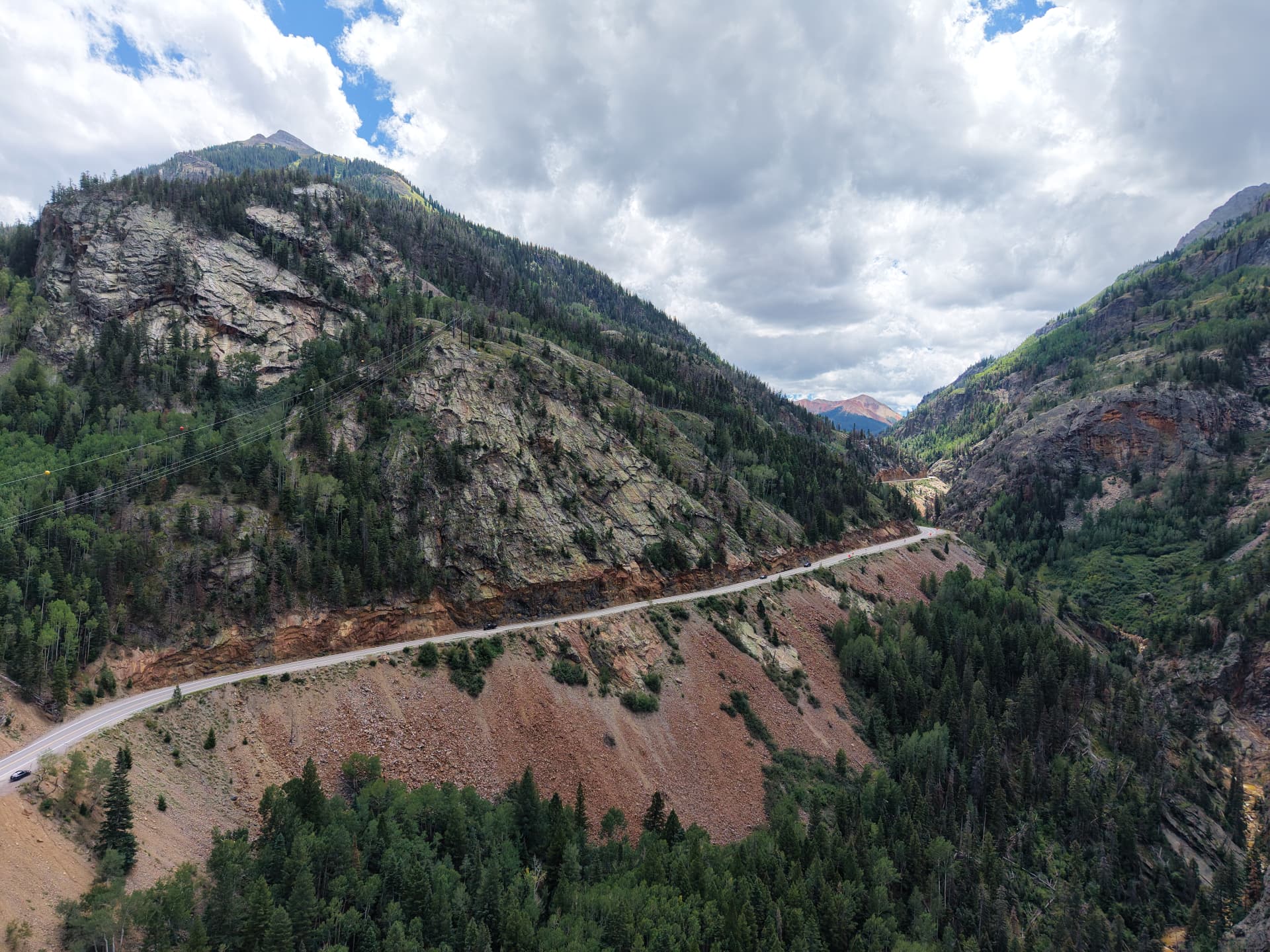 Aerial view of a winding highway cutting through the rocky mountains and green forests on the drive to Ouray, Colorado