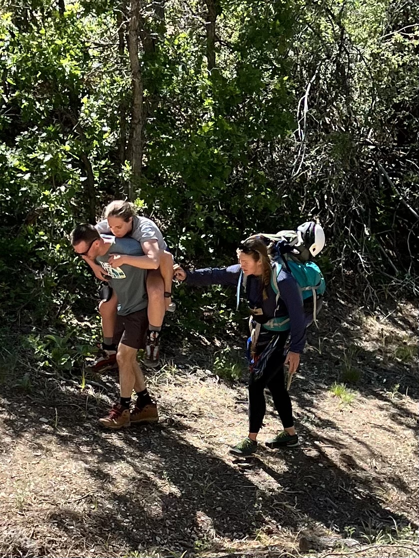 Jake carrying Brittany on his back down the trail after the via ferrata while the guide walks alongside