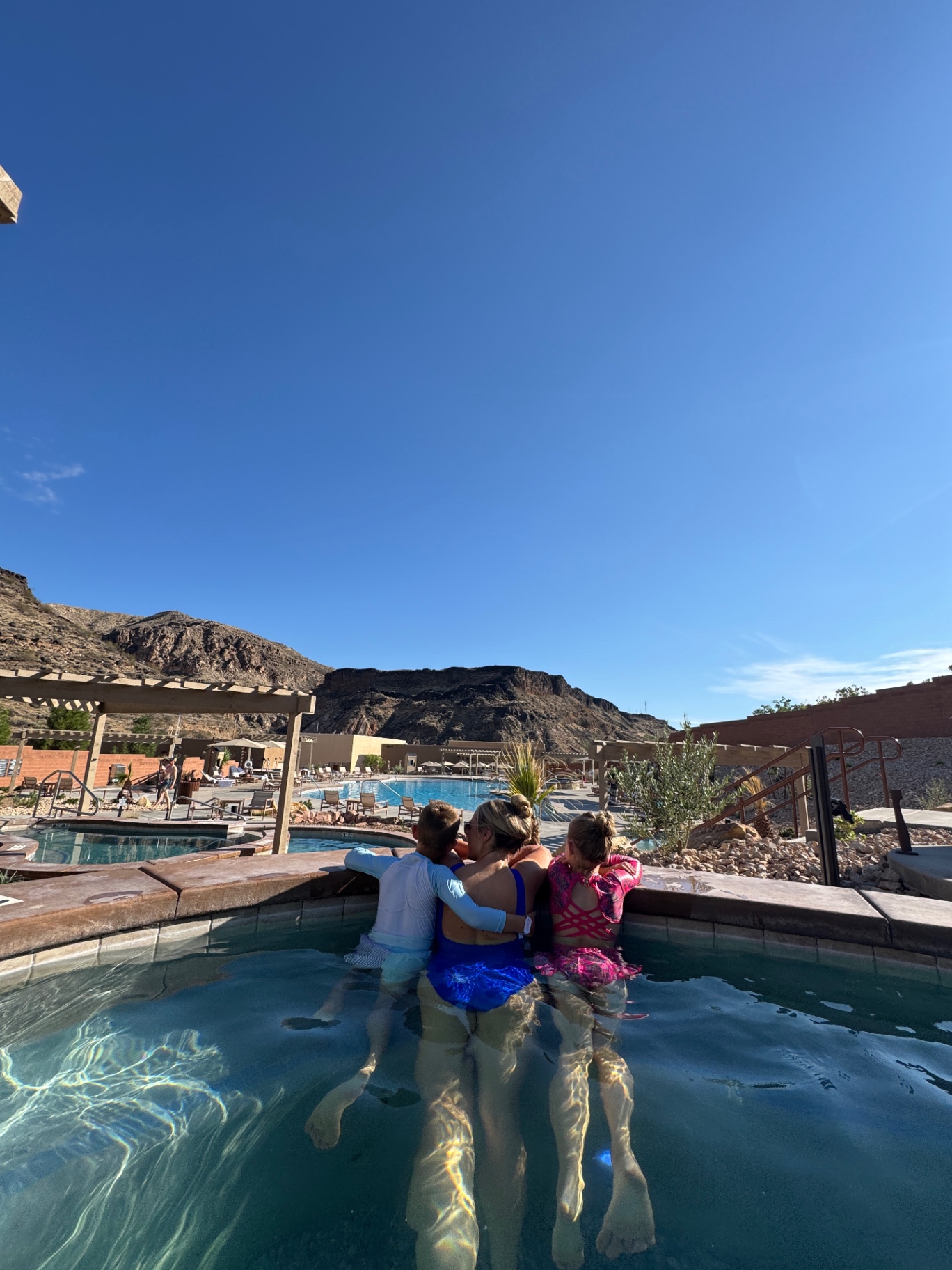 Brittany and the kids sitting on the edge of a soaking pool at Zion Canyon Hot Springs looking out at the red rock mountains