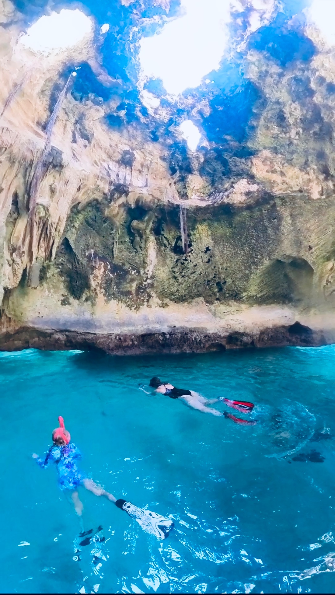 Snorkelers floating inside Thunderball Grotto with shafts of sunlight pouring through the cave roof