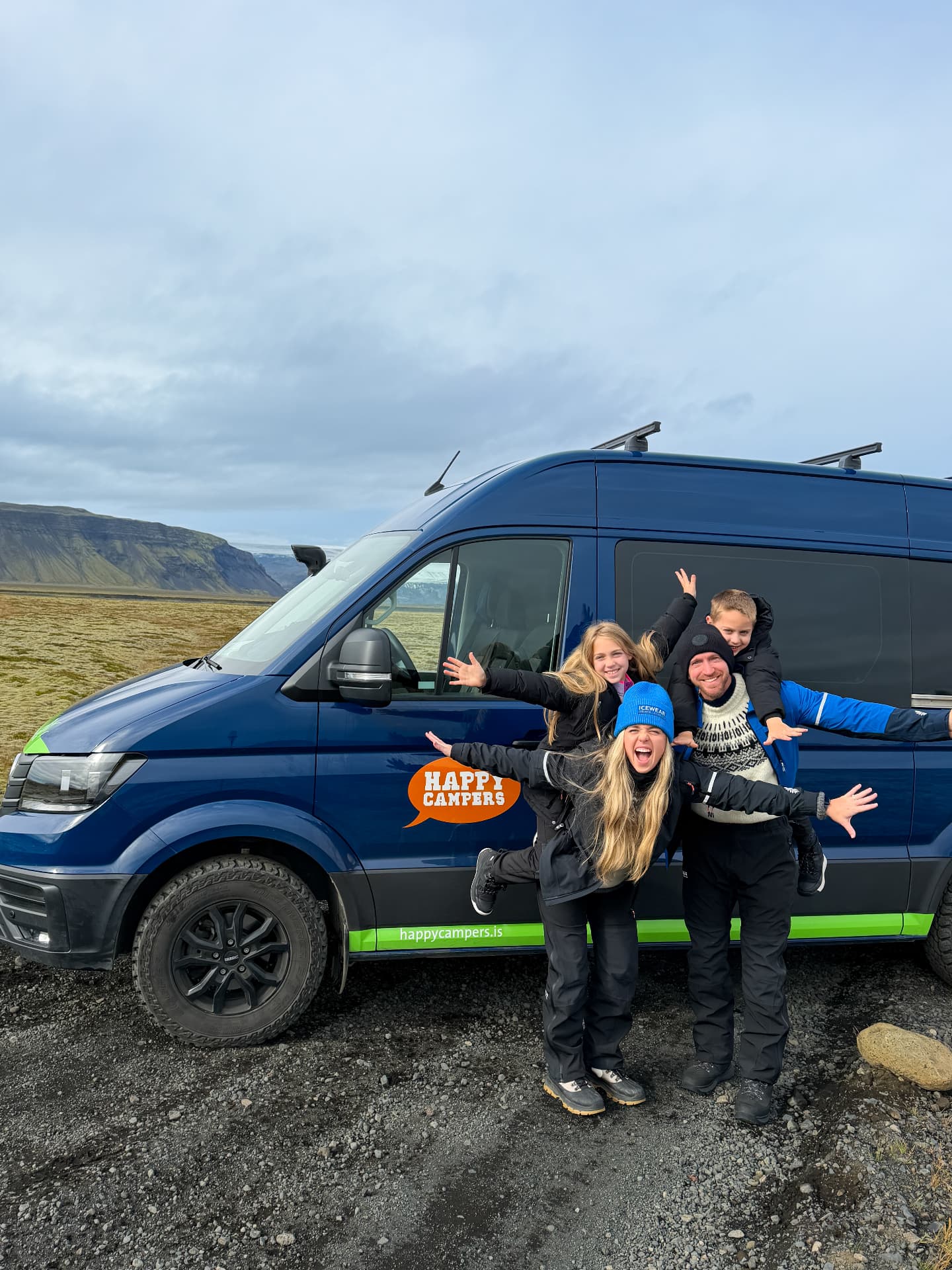 Brittany, Jake, Aniston, and Noah posing in front of a blue Happy Campers 4x4 XL van in Iceland