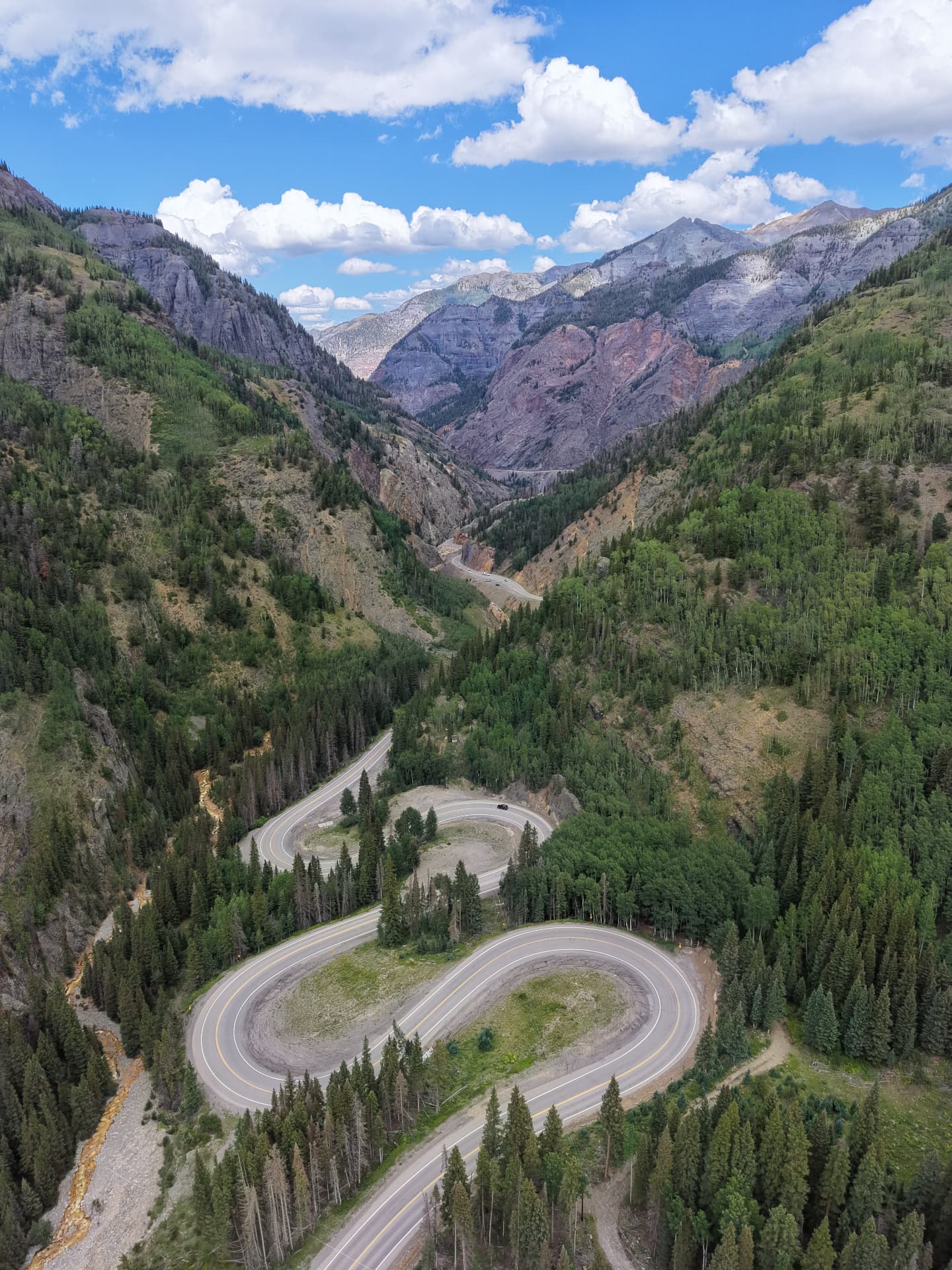 Aerial view of the Million Dollar Highway switchbacks winding through the green San Juan Mountains near Ouray, Colorado