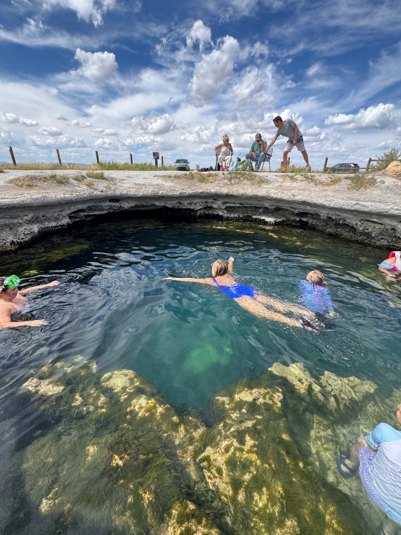 Crystal-clear blue water of the big pool at Meadow Hot Springs in Utah with swimmers and a wide-open desert sky overhead