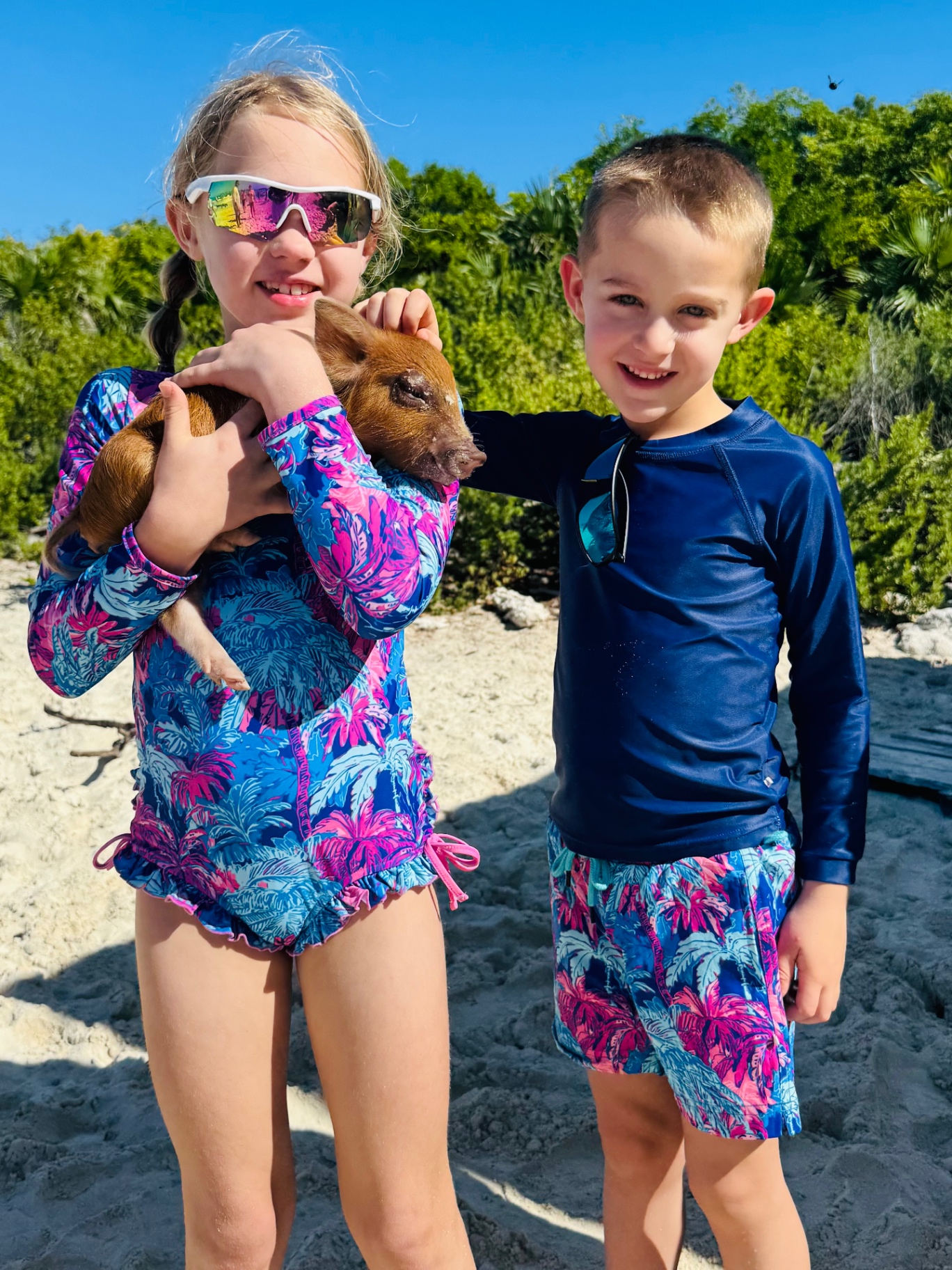 Aniston and Noah on the beach holding a small brown piglet on Pig Island, Exuma