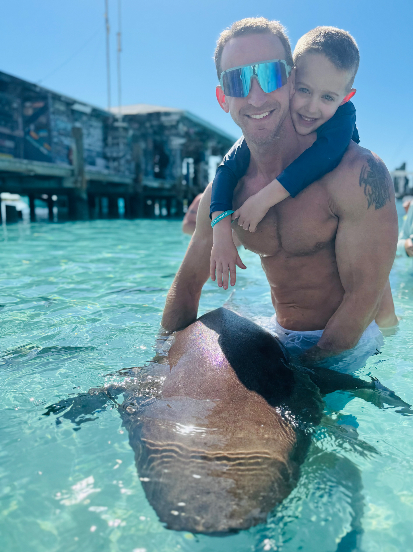 Jake holding Noah in the turquoise water next to a nurse shark at the Exuma Water Sports dock