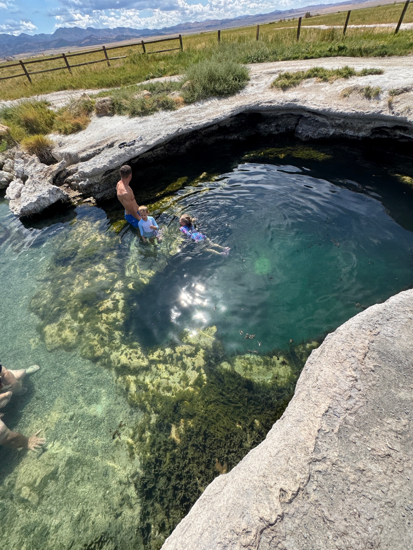Overhead view of Meadow Hot Springs with Jake and Noah wading in the clear turquoise water, mossy rocks below and Utah desert mountains in the distance